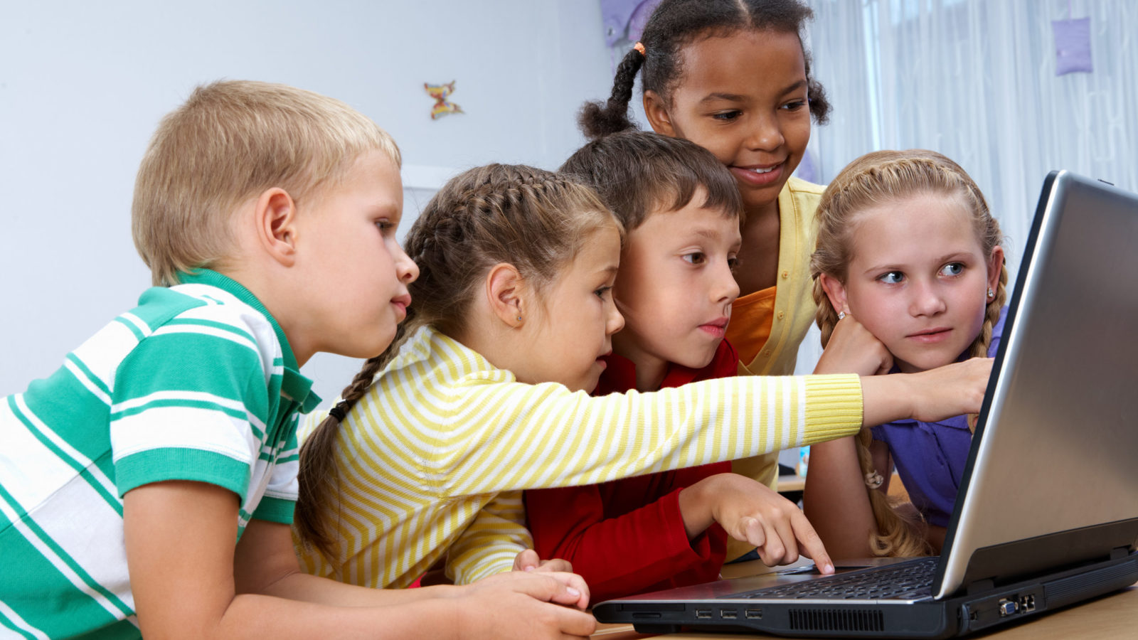 Portrait of elementary school students gathered around a laptop.