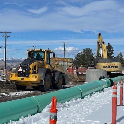 Liquor Warehouse construction site during winter of 2024. Large green pipes rest beside the snow in front of a yellow excavator.