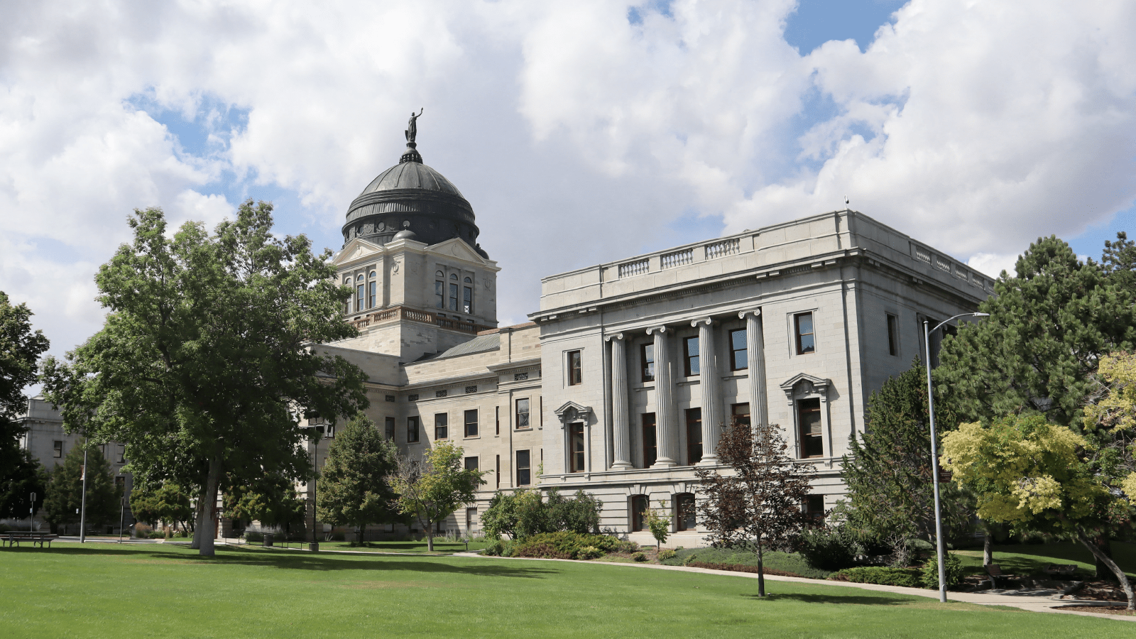 Image of the Montana State Capitol building, showcasing its neoclassical architecture with a prominent dome and statue atop, surrounded by lush greenery and a clear blue sky. Click to visit the Tax Simplification Hub.