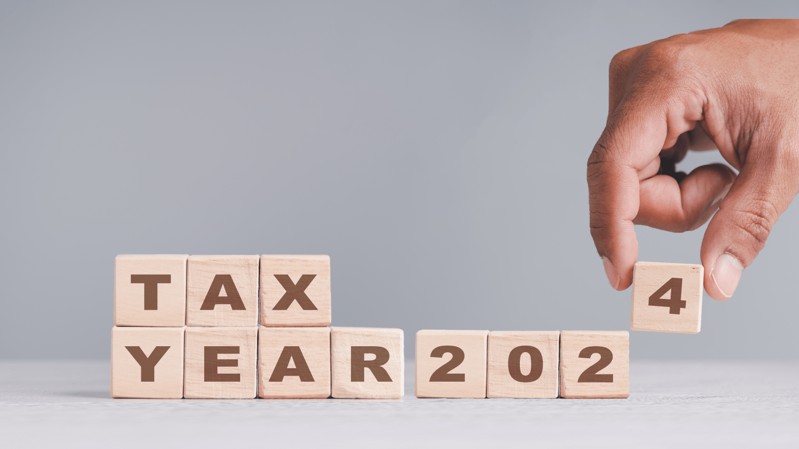 A hand placing the last of wooden blocks in a series, spelling out 'TAX YEAR 2024' on a light gray surface.
