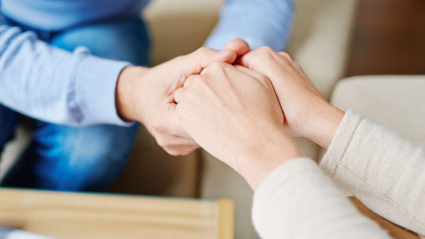 Close-up of a professional comforting a client by holding their hands during a consultation, symbolizing support and guidance in tax-related matters.