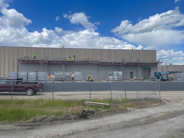 A wide view of the liquor warehouse construction site, showing workers on a scaffold working on the masonry wall.