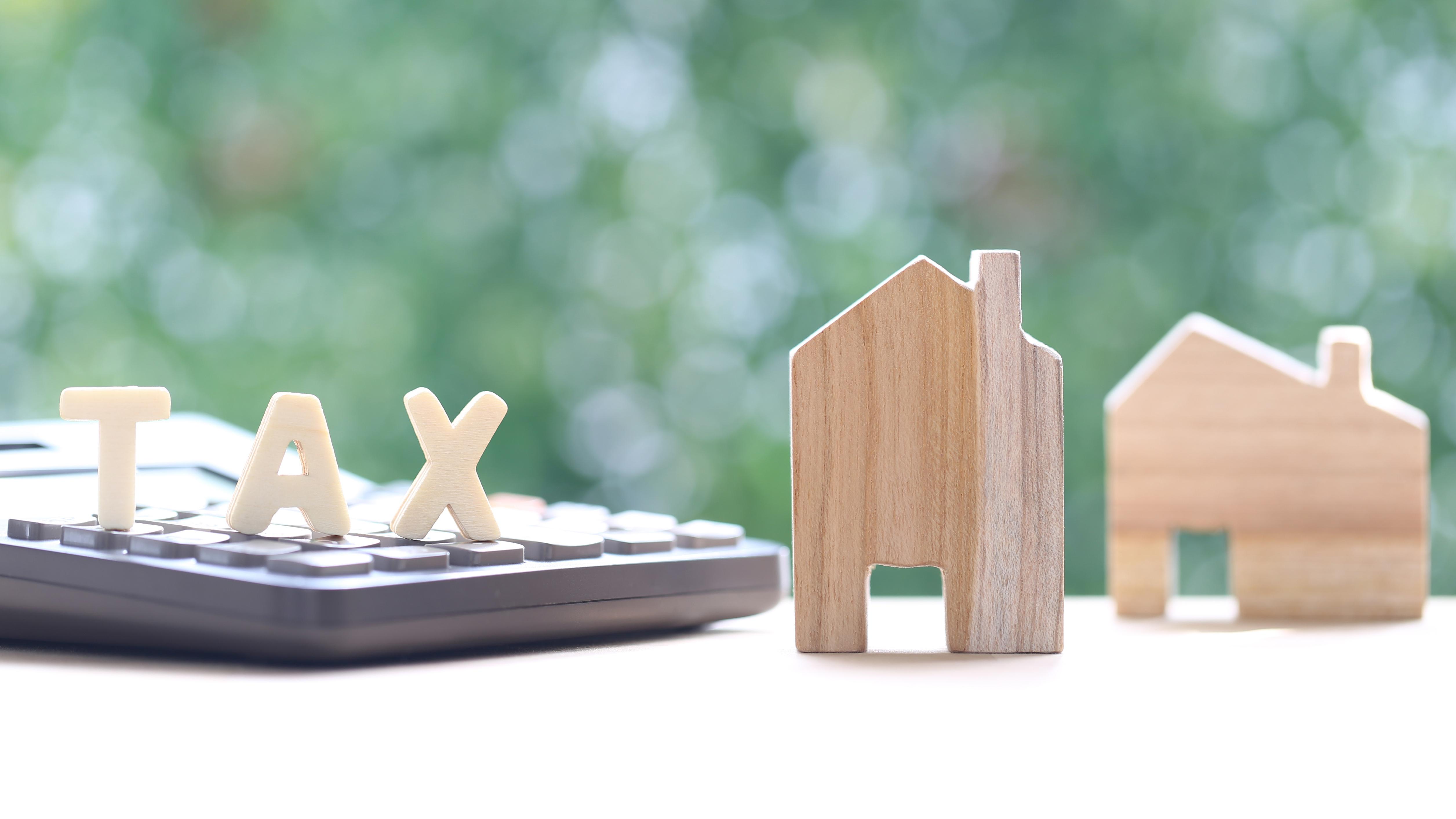 Model houses with tax word on calculator on green background